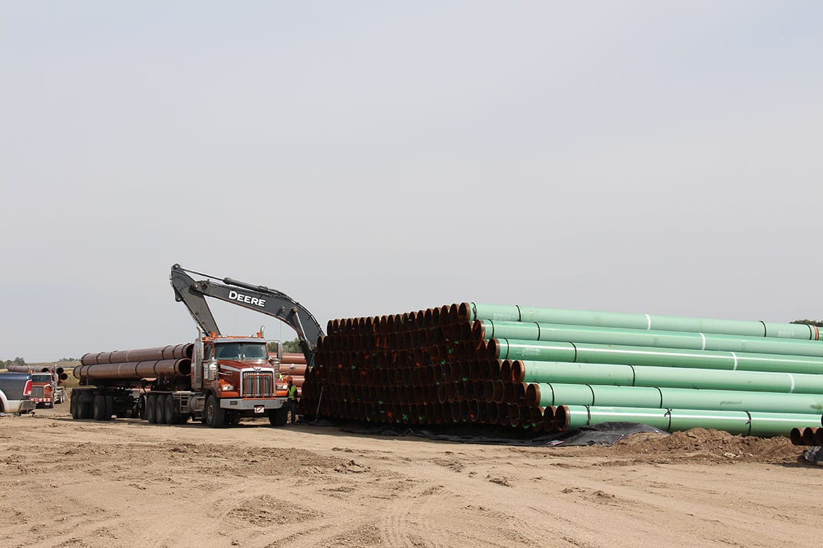 Construction equipment working near a large stack of green pipe